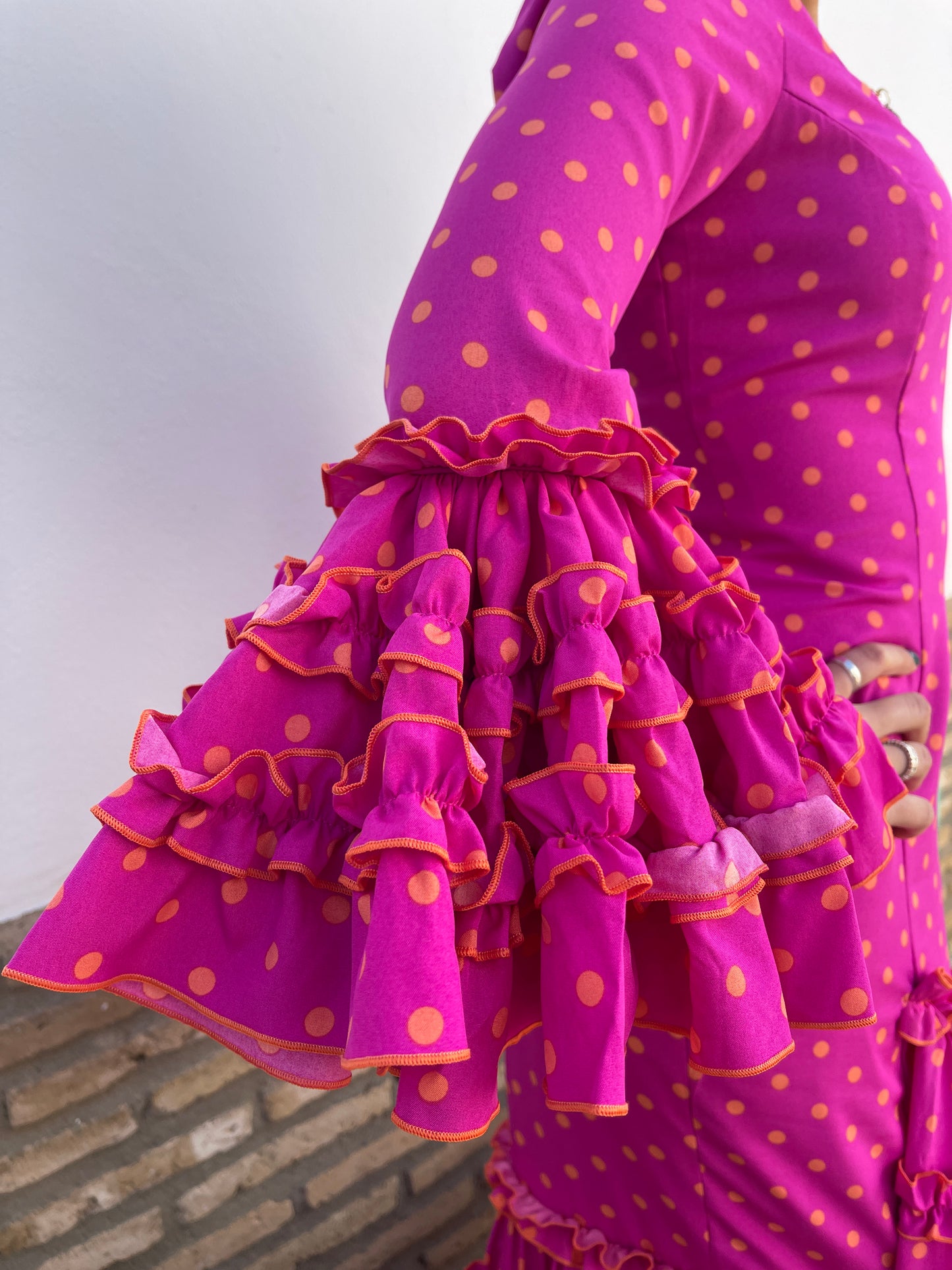 Traje de mujer para la feria. Detalle de los volantes de la manga del vestido de flamenca de mujer rosa fucsia con lunares naranja.