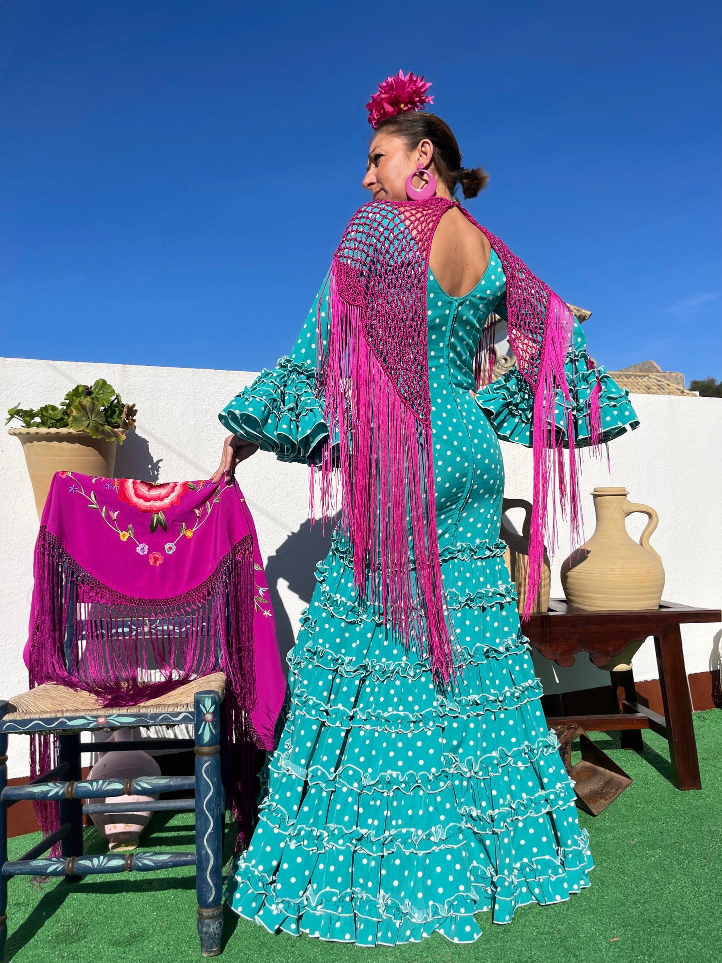 Vestido de sevillana turquesa con manga con volantes y patrón canastero. Ideal para ser una flamenca de sevilla. El look flamenco va con complementos como un manton de crochet buganvilla, flor buganvilla y pendiente de flamenca rosa.