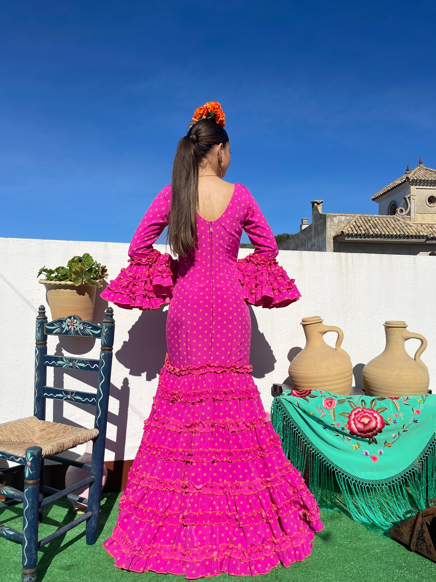 Parte trasera de vestido de flamenca de mujer de corte canastero rosa fucsia con lunares naranjas. Cierre con cremallera y cordón en el escote. Traje de flamenca ideal para la feria de abril.
