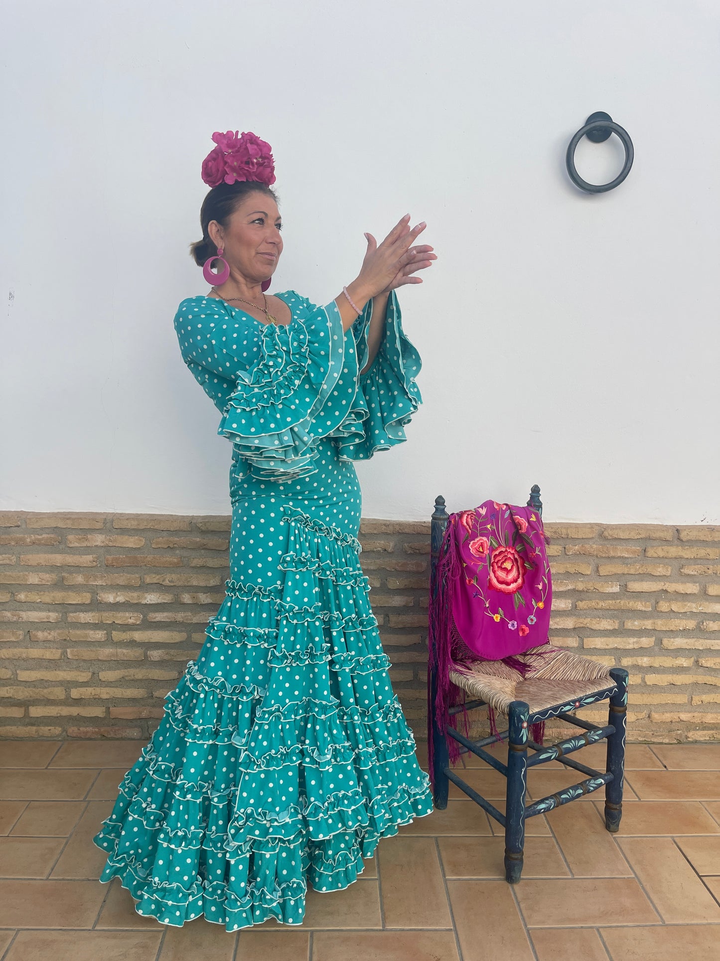 Flamenca sevilla con traje de manga volante de patrón canastero en color turquesa con lunares blancos. Este modelo es el traje de sevillana de la temporada flamenca 2024. Como complemento lleva un ramillete buganvilla y un mantoncillo buganvilla bordado de flores