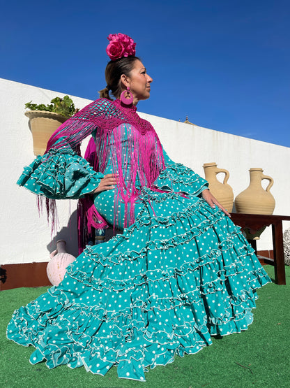 Yerbabuena moda también es una tienda del rocío online. Vendemos moda flamenca. Lleva un vestido turquesa con lunares blancos y volantes con corte canastero.